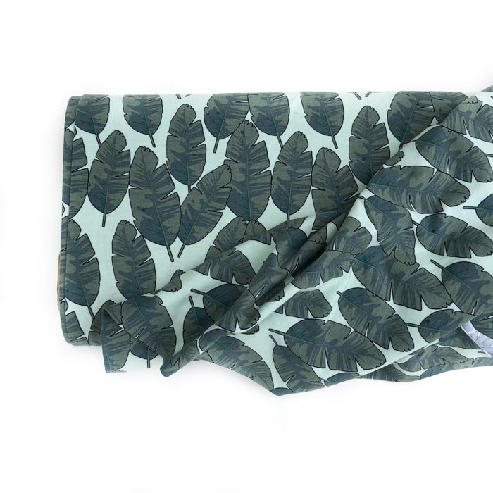 Elvelyckan banana leaf Neo Mint organic jersey cotton knit fabric.  With green banana leaves on a light green background