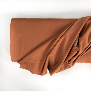 Photo of a roll of Family Fabrics solid cotton jersey cotton knit fabric in colour pecan. A medium brown colour